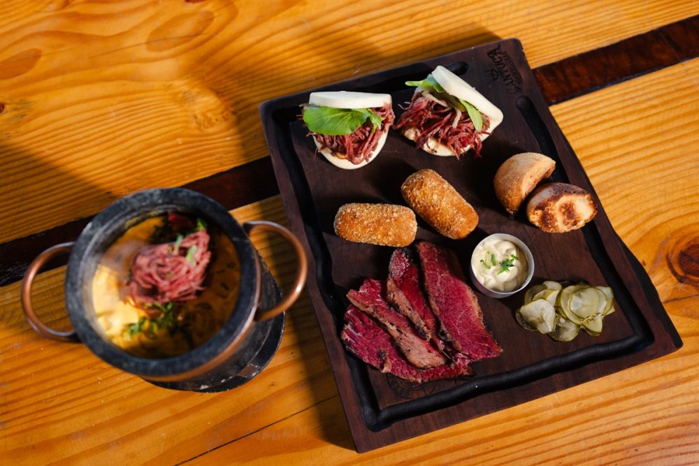 O pastrami, que conquistou espaço na gastronomia contemporânea brasileira graças ao preparo artesanal e ao sabor marcante, será o protagonista de um festival inédito em Curitiba. Até o fim de setembro, o Cantuca Brasero & Bar promove, todas as quartas-feiras, o Festival do Pastrami, reunindo uma experiência gastronômica pensada para quem deseja conhecer diferentes formas de apreciar a carne defumada. Servida exclusivamente às quartas-feiras, a tábua do festival reúne uma dupla de bão de pastrami, fondue de pastrami e abóbora cabotiá com três queijos, dupla de croquetas de pastrami, pastrami fatiado, picles, maionese Dijon e pão tostado. A experiência custa R$ 129 e serve de duas a três pessoas.
