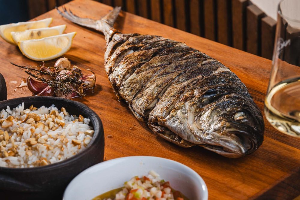 Do mar para a câmara de maturação e, depois, direto para a parrilla. Esse é o percurso de uma das principais atrações do Nacional Bar & Mar: os peixes inteiros assados na brasa. Inaugurado há três meses no Batel, o restaurante e gastrobar reúne no cardápio uma grande variedade de pescados do litoral brasileiro, preparados na tradicional churrasqueira depois de passarem pelo dry fish — processo de maturação a seco que vem conquistando chefs ao redor do mundo.